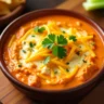 Creamy buffalo chicken dip in a ceramic baking dish surrounded by chips and vegetables for dipping